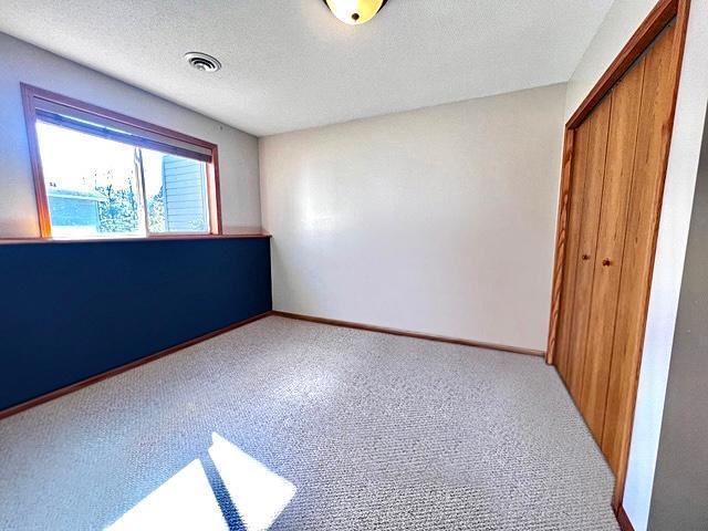 unfurnished bedroom featuring a textured ceiling, carpet flooring, visible vents, baseboards, and a closet