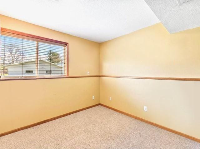 empty room featuring light colored carpet, a textured ceiling, and baseboards