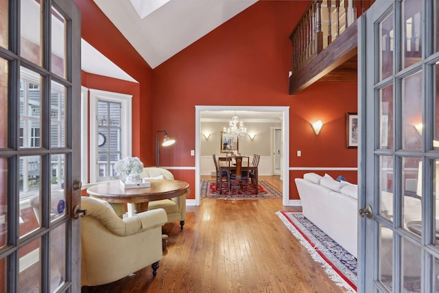 living area with high vaulted ceiling, plenty of natural light, hardwood / wood-style floors, and an inviting chandelier