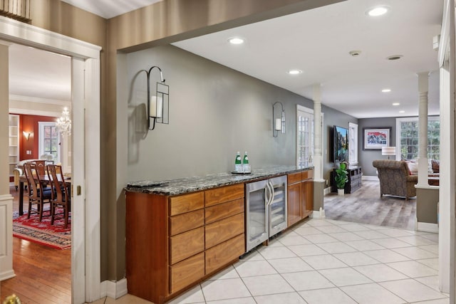 bar with ornamental molding, dark stone counters, wine cooler, light hardwood / wood-style floors, and a chandelier