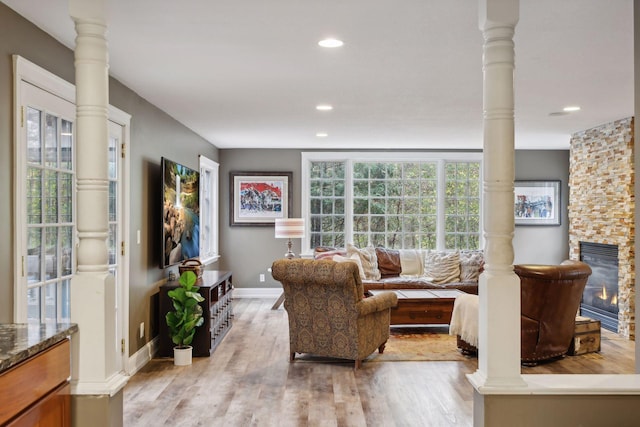 living room with light wood-type flooring, ornate columns, and a fireplace