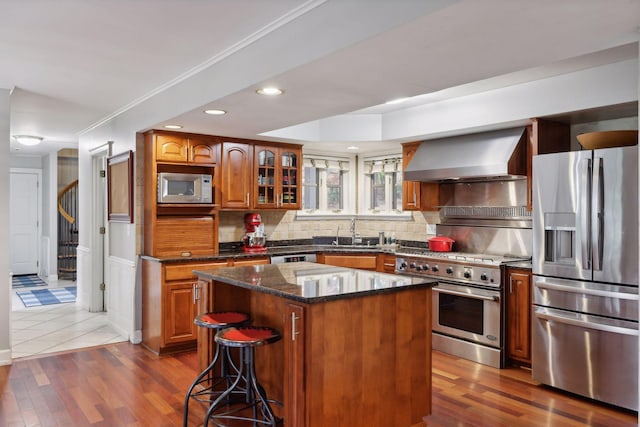 kitchen featuring wall chimney range hood, appliances with stainless steel finishes, dark wood-type flooring, and a kitchen island