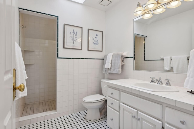 bathroom featuring tile patterned flooring, a tile shower, vanity, toilet, and tile walls