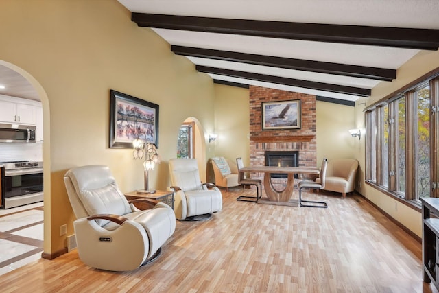 living room with a brick fireplace, light hardwood / wood-style flooring, and vaulted ceiling with beams