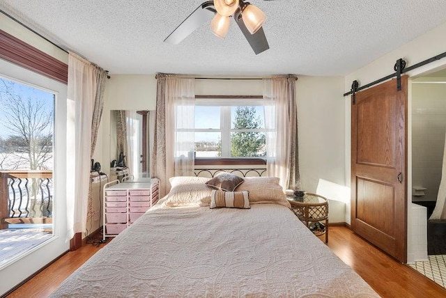 bedroom with ceiling fan, a barn door, hardwood / wood-style floors, and multiple windows