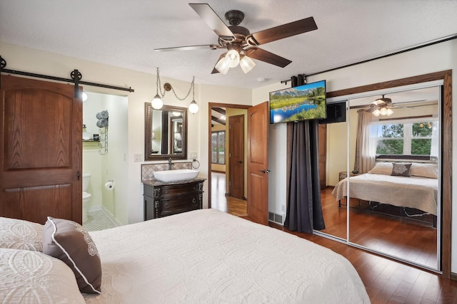 bedroom featuring a textured ceiling, a barn door, sink, a closet, and ceiling fan