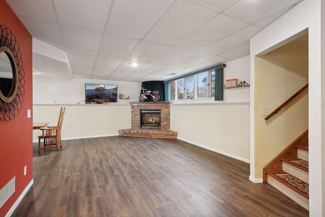 unfurnished living room with a fireplace, a drop ceiling, and dark hardwood / wood-style floors