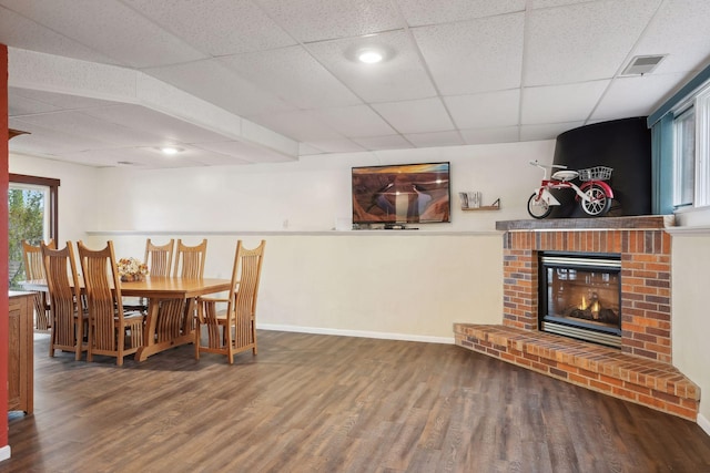 dining room featuring a brick fireplace, hardwood / wood-style floors, and a paneled ceiling