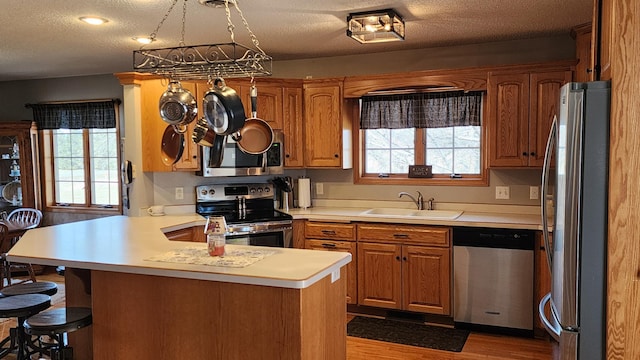 kitchen with hardwood / wood-style flooring, kitchen peninsula, stainless steel appliances, sink, and a textured ceiling