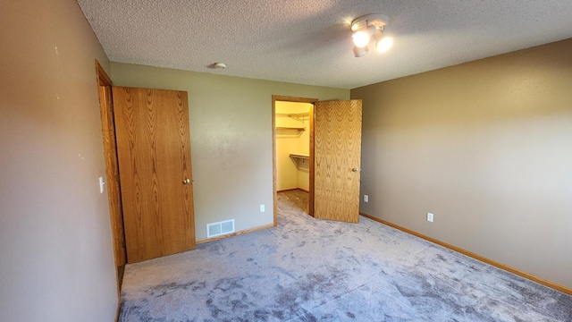 unfurnished bedroom with a closet, a textured ceiling, a spacious closet, and light colored carpet