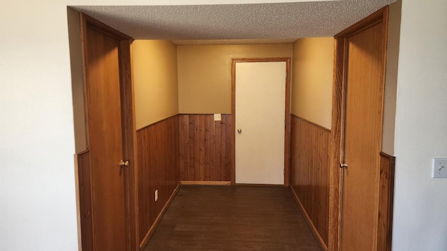 hall featuring dark wood-type flooring, a textured ceiling, and wood walls