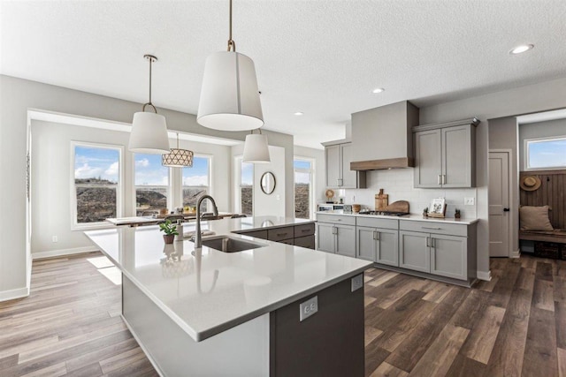 kitchen featuring pendant lighting, custom exhaust hood, sink, and a large island with sink