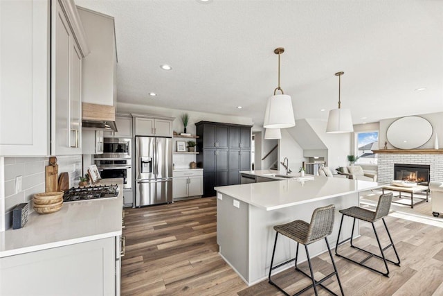 kitchen featuring a breakfast bar, hanging light fixtures, gray cabinets, an island with sink, and appliances with stainless steel finishes