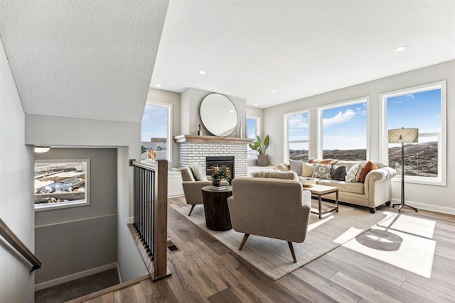 living room featuring wood-type flooring, a textured ceiling, a wealth of natural light, and a brick fireplace