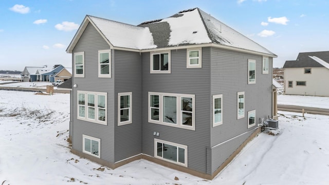 snow covered rear of property featuring central AC unit