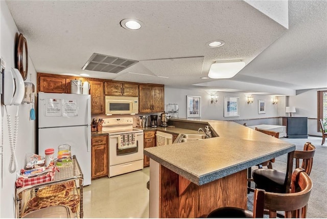 kitchen featuring white appliances, sink, a textured ceiling, kitchen peninsula, and a breakfast bar