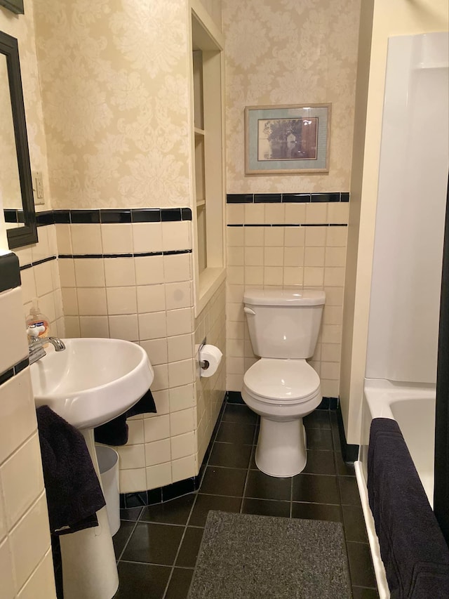 bathroom featuring sink, a tub, toilet, tile patterned floors, and tile walls