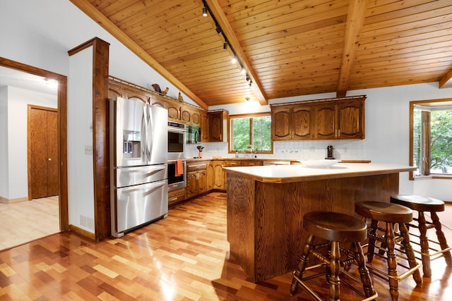 kitchen featuring kitchen peninsula, track lighting, appliances with stainless steel finishes, light wood-type flooring, and vaulted ceiling with beams