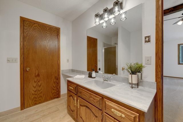 bathroom with wood-type flooring, a textured ceiling, ceiling fan, walk in shower, and vanity