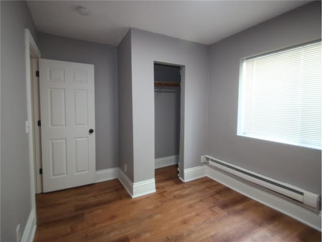 unfurnished bedroom with a closet, a baseboard heating unit, and hardwood / wood-style floors