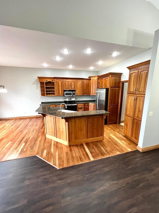 kitchen featuring appliances with stainless steel finishes, an island with sink, a kitchen bar, dark stone counters, and hardwood / wood-style flooring