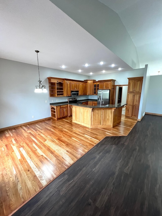 kitchen with lofted ceiling, a center island with sink, decorative light fixtures, appliances with stainless steel finishes, and light hardwood / wood-style floors