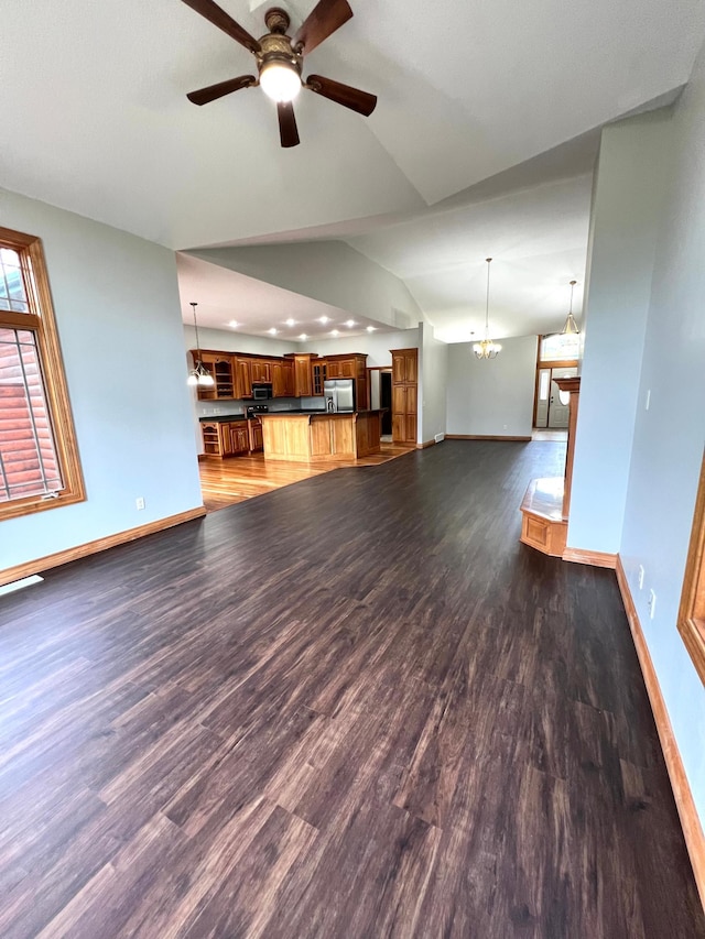 unfurnished living room with lofted ceiling, ceiling fan with notable chandelier, and dark hardwood / wood-style flooring