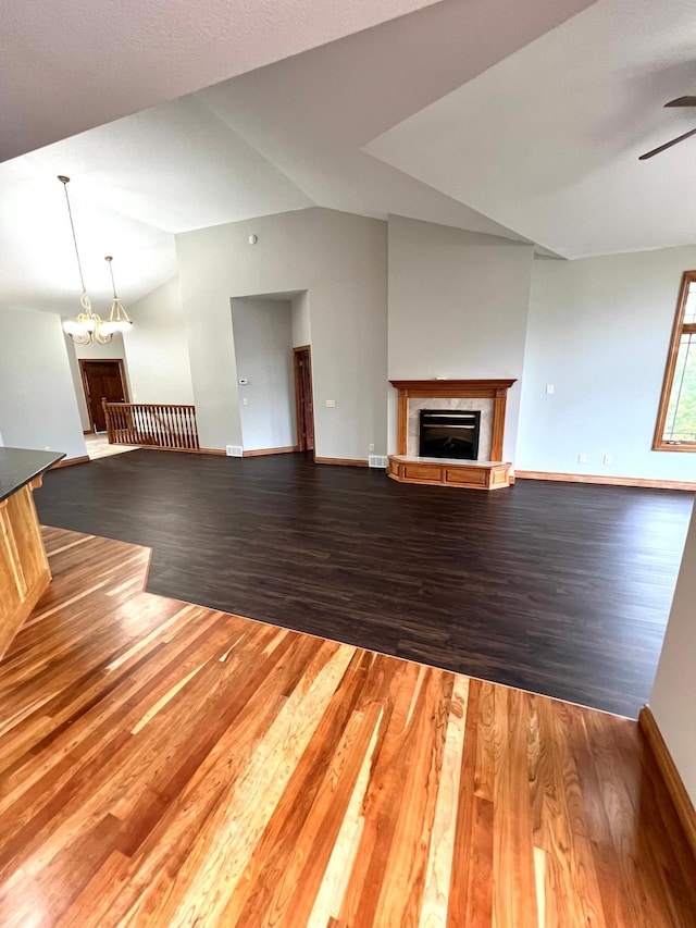 unfurnished living room featuring ceiling fan with notable chandelier, vaulted ceiling, a fireplace, and hardwood / wood-style floors