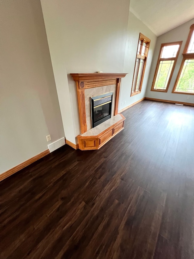 unfurnished living room with lofted ceiling, a tiled fireplace, and dark hardwood / wood-style flooring