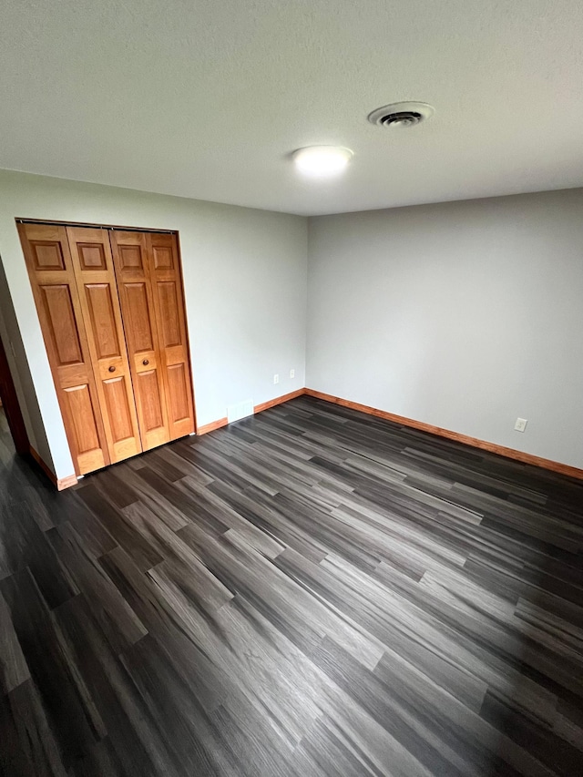 unfurnished bedroom with a closet, a textured ceiling, and dark hardwood / wood-style floors