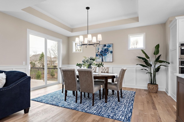 dining area with a raised ceiling, ornamental molding, an inviting chandelier, and light wood-type flooring