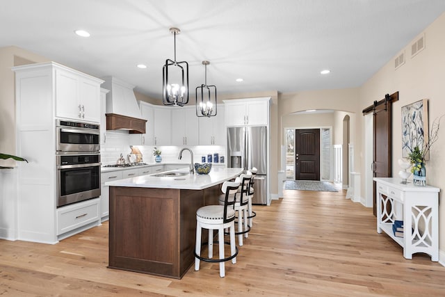 kitchen with sink, a barn door, premium range hood, appliances with stainless steel finishes, and light hardwood / wood-style floors