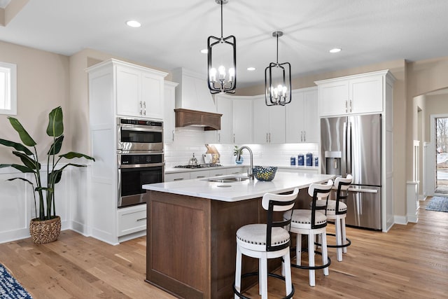 kitchen with light hardwood / wood-style flooring, stainless steel appliances, a center island with sink, sink, and white cabinets