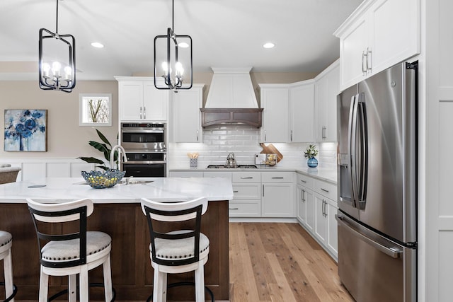 kitchen featuring custom exhaust hood, a breakfast bar area, white cabinetry, light wood-type flooring, and stainless steel appliances