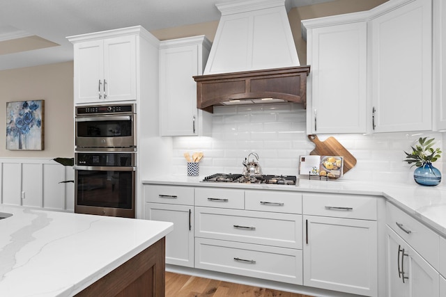 kitchen featuring custom exhaust hood, white cabinetry, appliances with stainless steel finishes, and light hardwood / wood-style floors