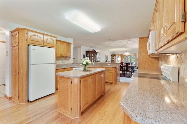 kitchen with white appliances, light hardwood / wood-style flooring, a kitchen island, decorative light fixtures, and kitchen peninsula