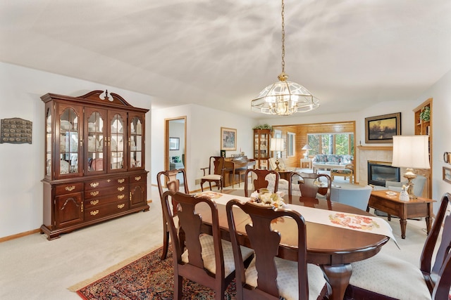 dining area featuring a tile fireplace, light carpet, and an inviting chandelier