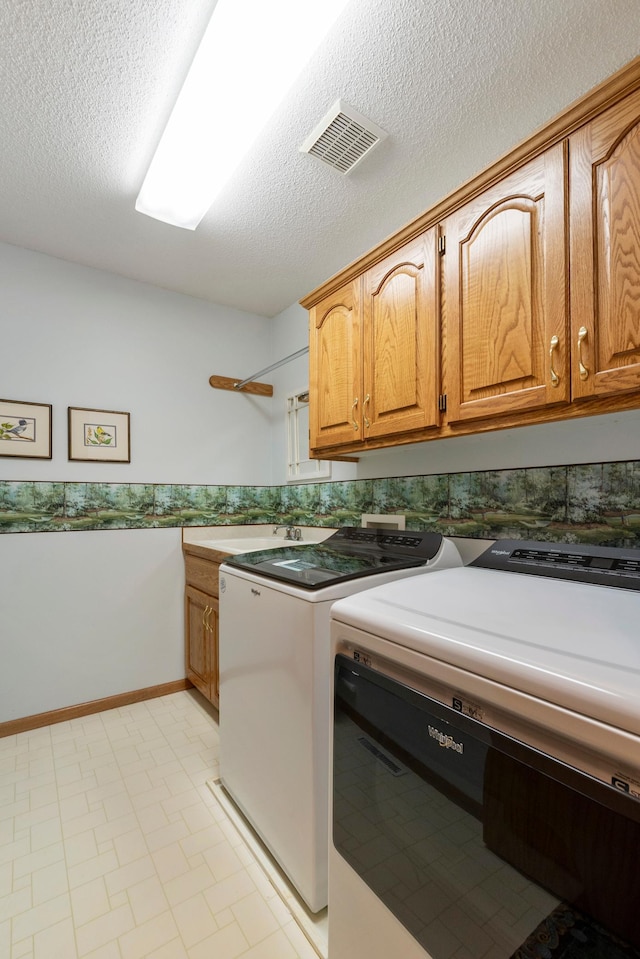 clothes washing area featuring sink, washing machine and dryer, cabinets, and a textured ceiling