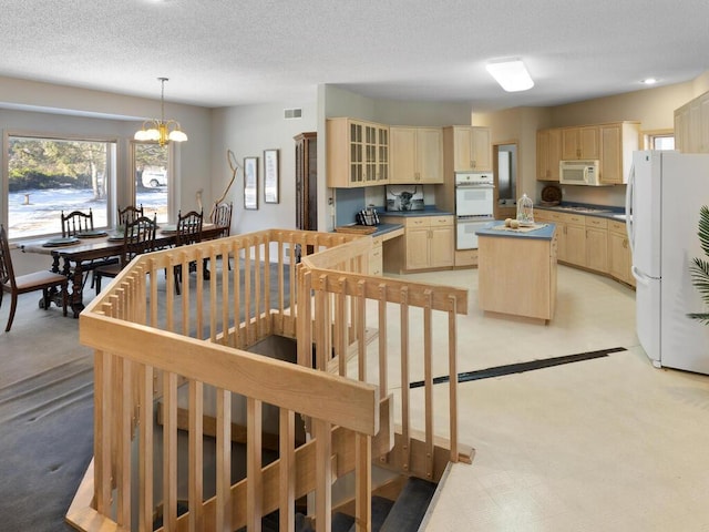 kitchen with a chandelier, a textured ceiling, a kitchen island, pendant lighting, and white appliances