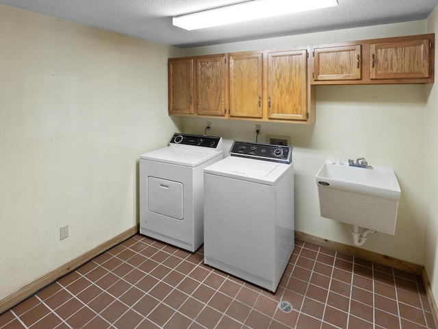 clothes washing area with cabinets, sink, washing machine and clothes dryer, and a textured ceiling