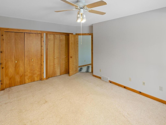 unfurnished bedroom featuring light carpet, ceiling fan, and multiple closets