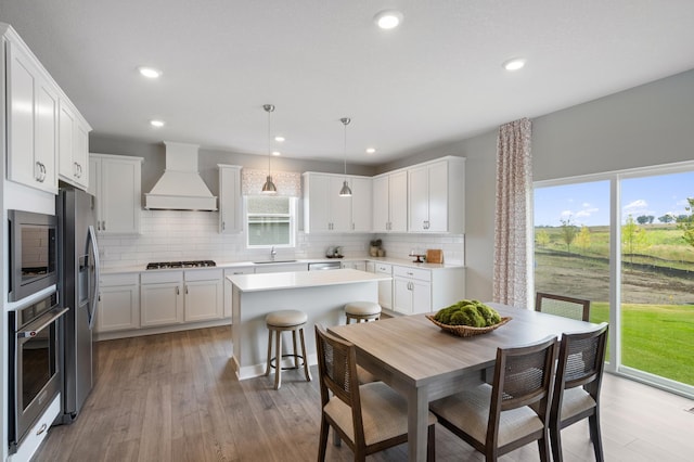 kitchen featuring light wood-type flooring, hanging light fixtures, stainless steel appliances, white cabinets, and custom range hood