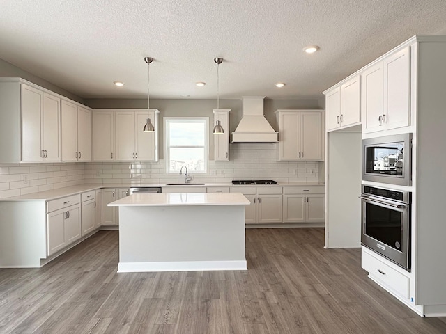 kitchen featuring stainless steel appliances, premium range hood, a sink, and light wood finished floors