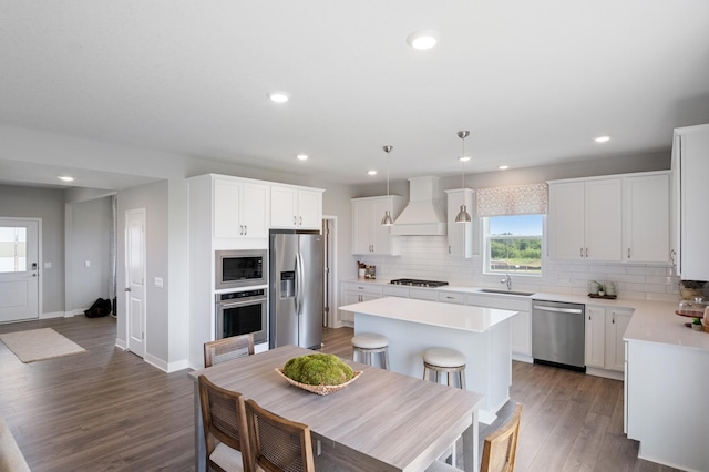 kitchen with tasteful backsplash, wood finished floors, custom exhaust hood, stainless steel appliances, and light countertops