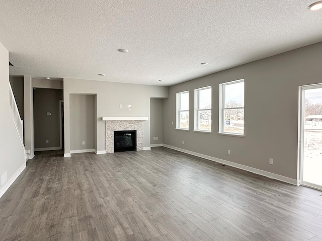 unfurnished living room with a textured ceiling, a stone fireplace, wood finished floors, and baseboards