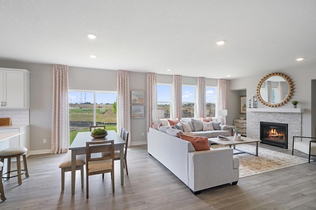 living area featuring light wood finished floors, recessed lighting, baseboards, and a stone fireplace