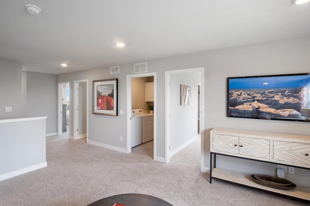 living room featuring light carpet, washer and clothes dryer, visible vents, and baseboards