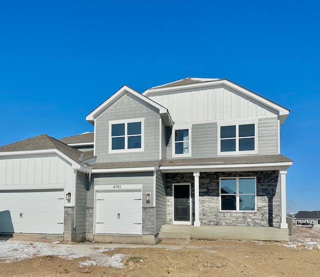 view of front of property with a garage, a shingled roof, stone siding, covered porch, and board and batten siding