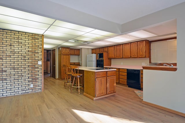 kitchen featuring a kitchen bar, black appliances, light hardwood / wood-style floors, a center island, and brick wall