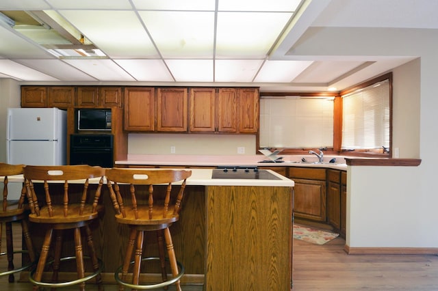 kitchen featuring black appliances, sink, a kitchen bar, and light wood-type flooring